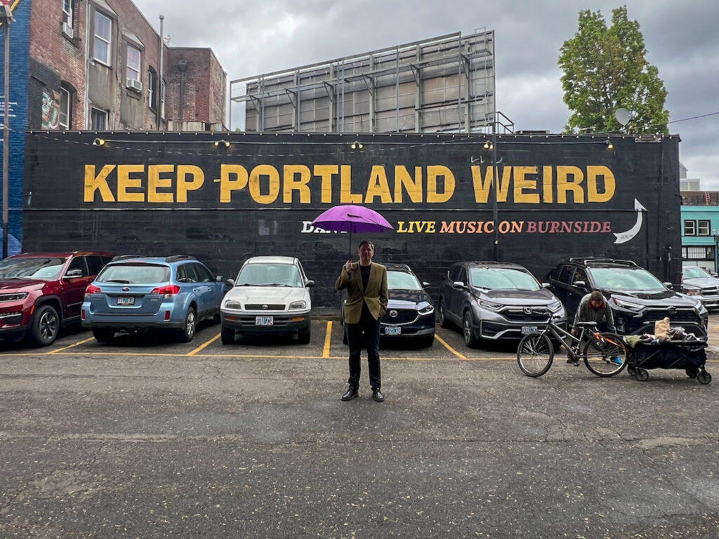 mann-vor-schriftzug-keep-portland-weird_foto-ralf-johnen Mann mit Regenschirm vor Schild mit der Aufschrift Keep Portland Weird