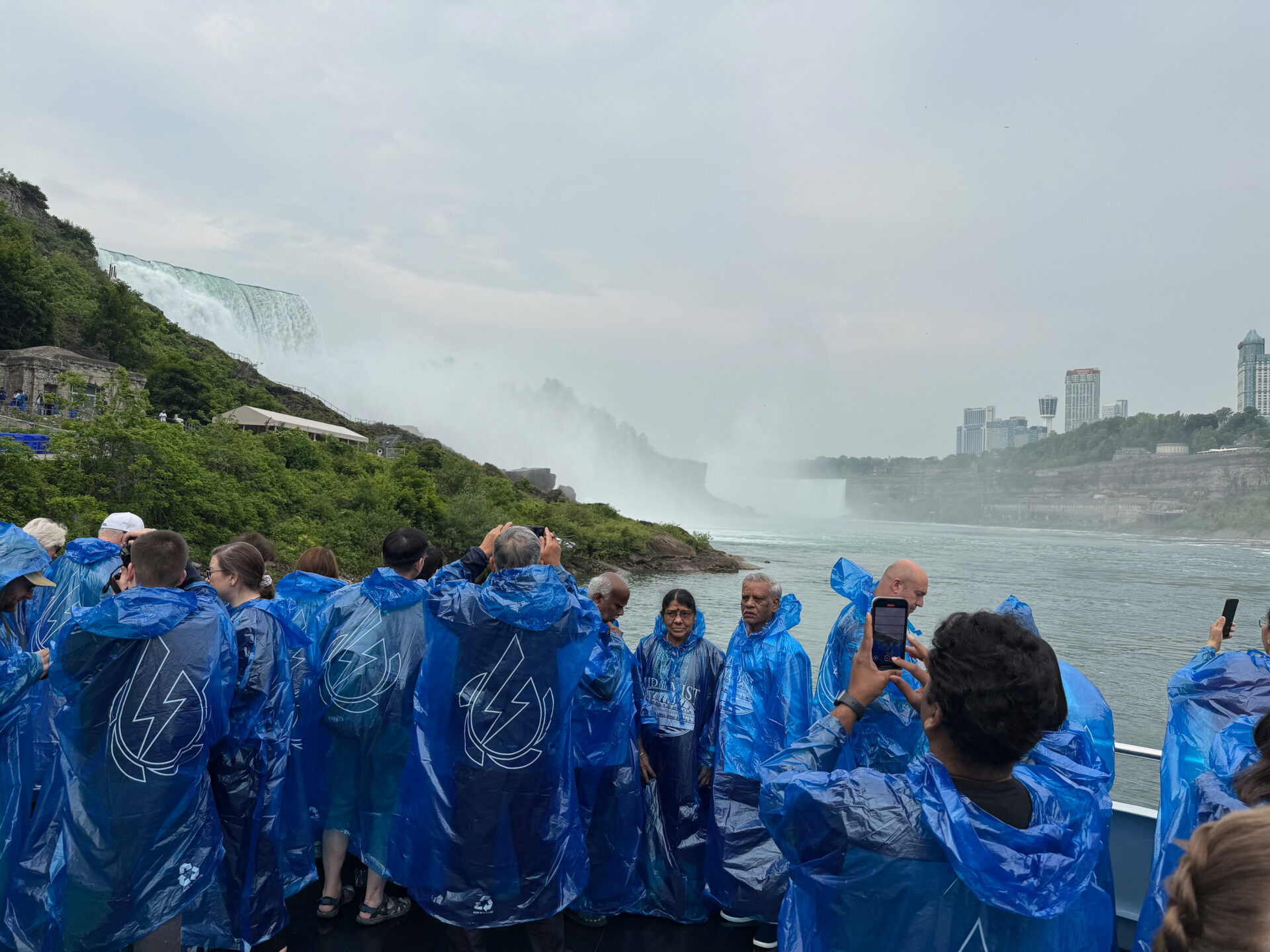 Passagiere der Maid of the Mist in blauen Ponchos vor den Niagarafällen