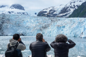 Touristen blicken durch Ferngläser auf eine Gletscherwand in Alaska