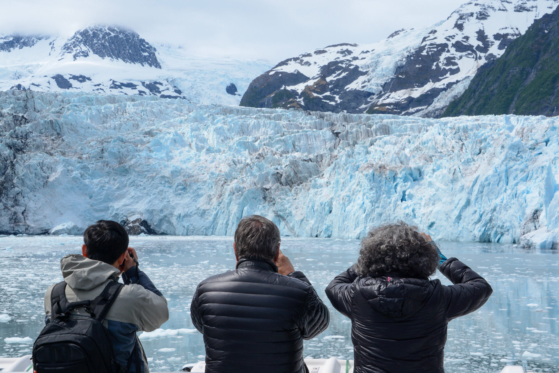 Touristen blicken durch Ferngläser auf eine Gletscherwand in Alaska