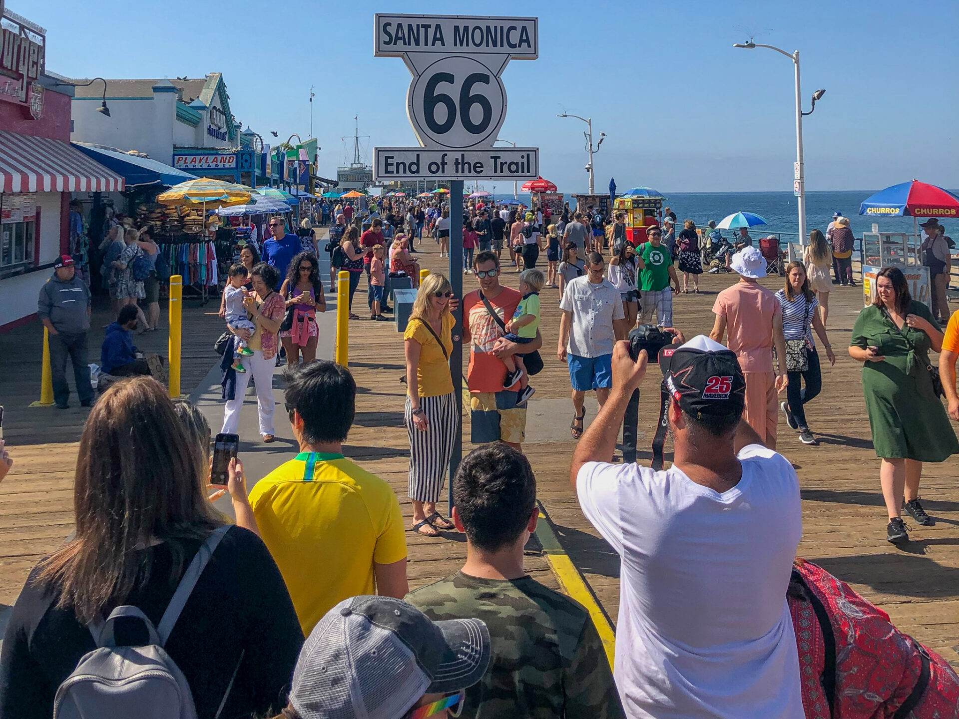 Touristen auf dem Santa Monica Pier fotografieren das Schild mit der Aufschrift "Santa Monica 66 End of the Trail"