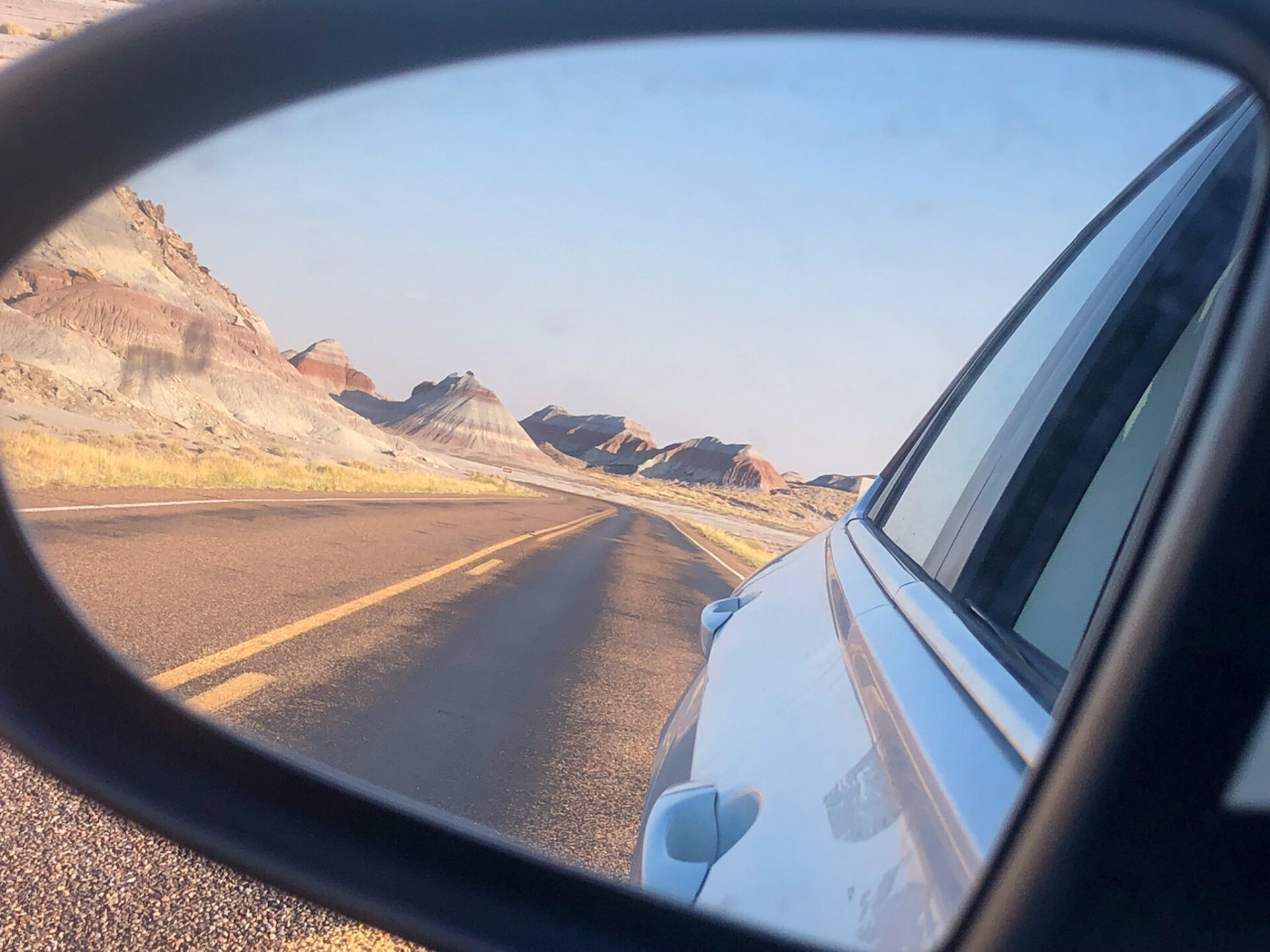 Blick auf die Painted Desert in Arizona und die verlassene Trasse der Route 66 durch den Rückspiegel eines Autos